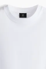 Remera de punto de algodón de peso medio, color blanco, con cuello redondo ribeteado, hombros caídos, bajo recto y corte relajado.