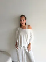 Conjunto de dos piezas compuesto por un top de corte asimétrico con escote amplio y mangas estilo capa, y un pantalón de corte recto y holgado. Ambas prendas están confeccionadas en tejido de lanilla gris.