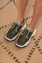 Championes urbanos de cuero verde con textura reptil, detalles en beige y amarillo, cordones negros y suela chunky blanca con base negra.