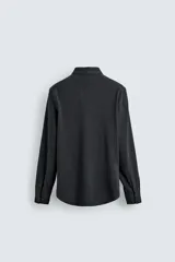 Camisa de corte relajado confeccionada en tejido de algodón con textura. Presenta cuello italiano, manga larga con puños abotonados y cierre frontal mediante botonadura.