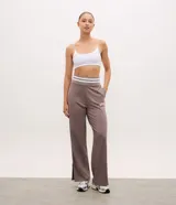 Pantalón deportivo de corte recto color marrón, confeccionado en una mezcla de modal y algodón. Presenta cintura elástica en rib con rayas blancas contrastantes, bolsillos laterales y detalle de lettering bordado en la pierna. Incluye aberturas laterales en el ruedo.