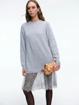 Sweater de punto gris de corte holgado y largo, con cuello redondo y mangas largas. Presenta un aplique de encaje semitransparente en el ruedo que le otorga un estilo femenino y delicado.