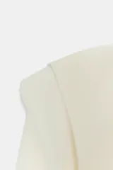 Jersey de punto de cuello redondo y manga larga, con diseño estructurado que incorpora hombreras marcadas y detalles de pliegues en los hombros.