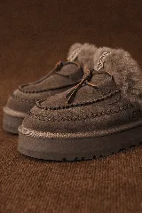 Pantuflas UGG de cuero color marrón con interior de piel sintética y detalle de costuras en contraste.