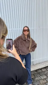 Chaqueta de piel sintética en color chocolate, con cuello clásico, cierre frontal metálico y bolsillos laterales. Presenta un diseño de corte holgado con ruedo ajustable mediante elástico.