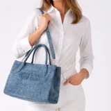 Cartera tipo tote de Guess confeccionada en tela denim con efecto lavado. Presenta el logo de la marca bordado en el frente, doble asa de mano y una correa larga ajustable y extraíble.