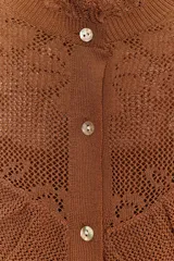 Chaqueta de punto pointelle color tostado, con cuello subido y manga larga. Presenta detalles de volantes en el pecho y puños, y cierre frontal con botones.