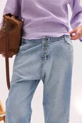Pantalón de jean de tiro bajo y calce relajado, con cierre frontal de múltiples botones visibles y largo al tobillo.