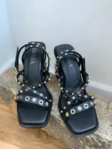 Sandalias negras con tiras finas adornadas con apliques metálicos y perlas. Taco de 9 cm y base cuadrada.