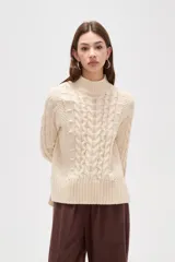 Polera de tejido de punto color crema, con cuello alto y diseño de trenzas verticales. Presenta mangas largas con puños acanalados y un corte holgado.