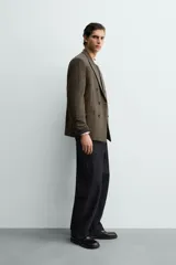 Blazer de corte relajado confeccionada en tejido con lana, con diseño de cuadros pequeños. Presenta cuello con solapas de pico, cierre frontal de botonadura cruzada, manga larga con botones en los puños y bolsillos de vivo en el pecho y la cadera.