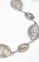 Cinto plateado con eslabones ovalados decorados con motivos florales y geométricos.