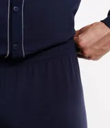 Pijama masculino de dos piezas en color azul marino. Incluye una camisa de manga larga con cuello en V, cierre frontal abotonado y detalles de costuras en contraste, junto con un pantalón de corte recto y cintura elástica.