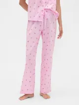 Pijama de dos piezas confeccionado en popelina, compuesto por una camisa de manga corta con cuello solapa y cierre frontal de botones, y un pantalón largo de corte recto con cintura elástica. Presenta un estampado integral de cerezas sobre fondo rosado.