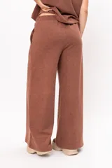 Pantalón de corte ancho y tiro alto, confeccionado en tejido de punto color marrón. Presenta cintura elástica y costuras verticales decorativas en el frente de cada pierna.