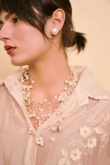 Collar de hilos finos entrelazados con múltiples perlas sintéticas y dijes florales y circulares dorados con esmalte blanco.