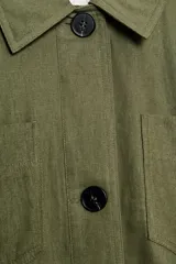 Cazadora verde militar de corte crop, confeccionada en hilatura con lino, con cuello solapa, manga larga y bolsillos de plastrón en el delantero. Cuenta con cierre frontal de botones oscuros y detalles a rayas en contraste en los puños y el interior.