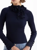 Sweater de tejido de punto fino color marrón, con ajuste al cuerpo, cuello alto con detalle de volados y moño, y mangas largas con puños acampanados con volados.