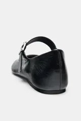 Bailarina plana de mujer, color negro charol, con punta ligeramente afilada y tira ajustable con hebilla metálica plateada sobre el empeine.