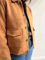 Chaqueta de estilo clásico con acabado efecto gamuza, confeccionada en algodón. Presenta cierre frontal con botones, cuello camisero y dos bolsillos delanteros con solapa. Posee interior forrado y corte recto.