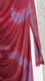 Vestido midi de microtul con diseño drapeado lateral, cuello alto y mangas largas. Presenta un estampado tipo tie-dye en tonos bordó y violeta.