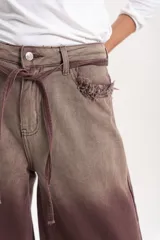 Jean wide leg de tiro medio con efecto desteñido en tono marrón y detalles desflecados en los bolsillos delanteros. Incluye un lazo de tela ajustable en la cintura.