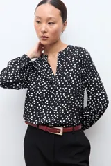 Blusa negra con estampado de lunares blancos, escote en V y mangas largas con puños abotonados.