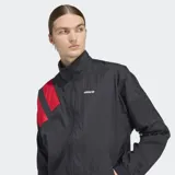 Campera deportiva Adidas de corte holgado, con cierre frontal de cremallera y cuello alto. Presenta un diseño en bloques de color negro con detalles en rojo en las mangas, confeccionada en tejido técnico reciclado.