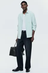 Camisa H&M de algodón Oxford con estampado de rayas verticales blancas y verdes, cuello americano, bolsillo frontal de parche y cierre central de botones.
