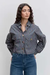 Camisa de corte oversize con diseño de rayas verticales en tonos azul y blanco, cuello clásico, cierre frontal con botones y mangas largas con puños abotonados.