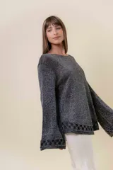 Sweater de tejido liviano con efecto lurex, color beige o gris claro metalizado. Presenta cuello redondo, mangas amplias estilo campana y terminaciones en punto elástico con diseño de cuadros en puños y ruedo.