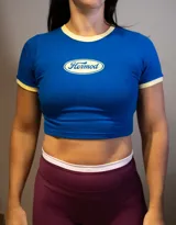 Remera corta de manga corta, color azul vibrante, con cuello redondo y ribetes en color crema. Presenta un logo ovalado centrado con el texto "Hermod" en tipografía cursiva.