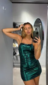 Vestido corto de lurex verde esmeralda, con breteles finos y corte ajustado. Presenta frunces laterales que realzan la figura.