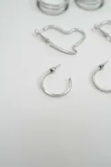 Set de tres pares de aros plateados de diferentes diseños: un par de aros tipo argolla doble, un par de aros con forma de corazón y un par de aros tipo argolla con textura estriada.