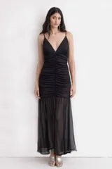 Vestido largo negro con breteles finos y escote en V. Presenta un diseño con frunce central en el torso que realza la silueta y una falda amplia con caída liviana y transparente en la parte inferior.