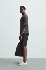 Bermuda negra de corte recto, con cintura elástica ajustable mediante cordón, pliegues frontales y bolsillos de vivo en la espalda. El bajo tiene un dobladillo vuelto.