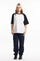 Remera de corte oversize con diseño tipo ranglan, que combina cuerpo blanco con mangas y cuello en color negro. Presenta un pequeño logo bordado en el centro del pecho.