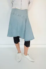 Falda midi de denim en tono azul claro, con tiro medio y diseño asimétrico con tablas laterales. Cuenta con cierre lateral mediante cremallera metálica.
