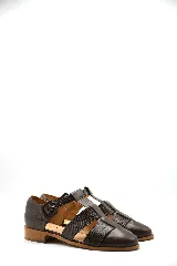 Zapato tipo cangrejera de cuero color marrón, con diseño de tiras entrelazadas, punta cerrada y pulsera con hebilla ajustable al tobillo. Cuenta con un taco bajo de madera.