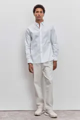 Camisa de manga larga en color blanco, con cuello clásico y cierre frontal de botones. Presenta un corte recto y un pequeño detalle bordado en la parte inferior.