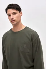 Remera de manga larga color verde oliva, confeccionada en algodón pesado con textura suave. Presenta un bolsillo frontal en el pecho con un pequeño bordado de la marca y puños acanalados en las mangas.