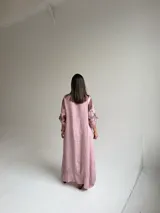 Vestido largo color rosa, con mangas cortas y diseño holgado, presenta un estampado floral en tonos marrones y verdes en un lateral, además de un bolsillo aplicado en la parte frontal y costuras visibles de estilo rústico.
