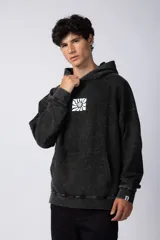 Buzo canguro con capucha, de calce oversize y efecto lavado gastado. Presenta un estampado gráfico central en color blanco y un pequeño parche con logo en el puño.
