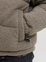 Campera puffer con diseño de bloques de color, combinando tejido teddy en tono arena y paneles negros en los hombros. Presenta cuello alto, cierre frontal y diseño acolchado.