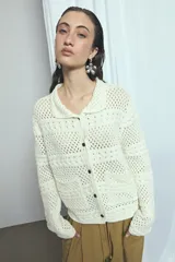 Cardigan de punto calado color marfil, con cuello solapa, cierre frontal de botones oscuros y bolsillos frontales.