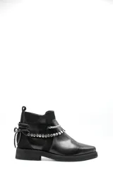 Bota corta tipo chelsea de cuero negro, con paneles laterales de gamuza y suela plana de goma. Presenta un diseño minimalista con tirador en la parte trasera.