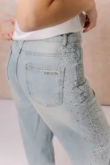 Jean wide leg tiro alto de lavado claro, con diseño de cinco bolsillos, cierre frontal con botón y aplicación de strass en degradé a lo largo de los laterales.