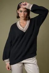 Buzo de punto en color azul marino con escote en V, puños y cuello con detalles en franjas de color turquesa y rojo. Presenta un diseño holgado de manga larga.