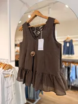 Blusa sin mangas color marrón oscuro con escote en V, volado peplum en el ruedo y detalle de lazos cruzados ajustables en la espalda. Incluye un collar artesanal con dije tejido.