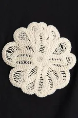 Remera negra de punto de algodón, de corte holgado con hombros caídos, cuello redondo acanalado y mangas cortas. Presenta dos apliques decorativos circulares de crochet en tono crudo a la altura del pecho.